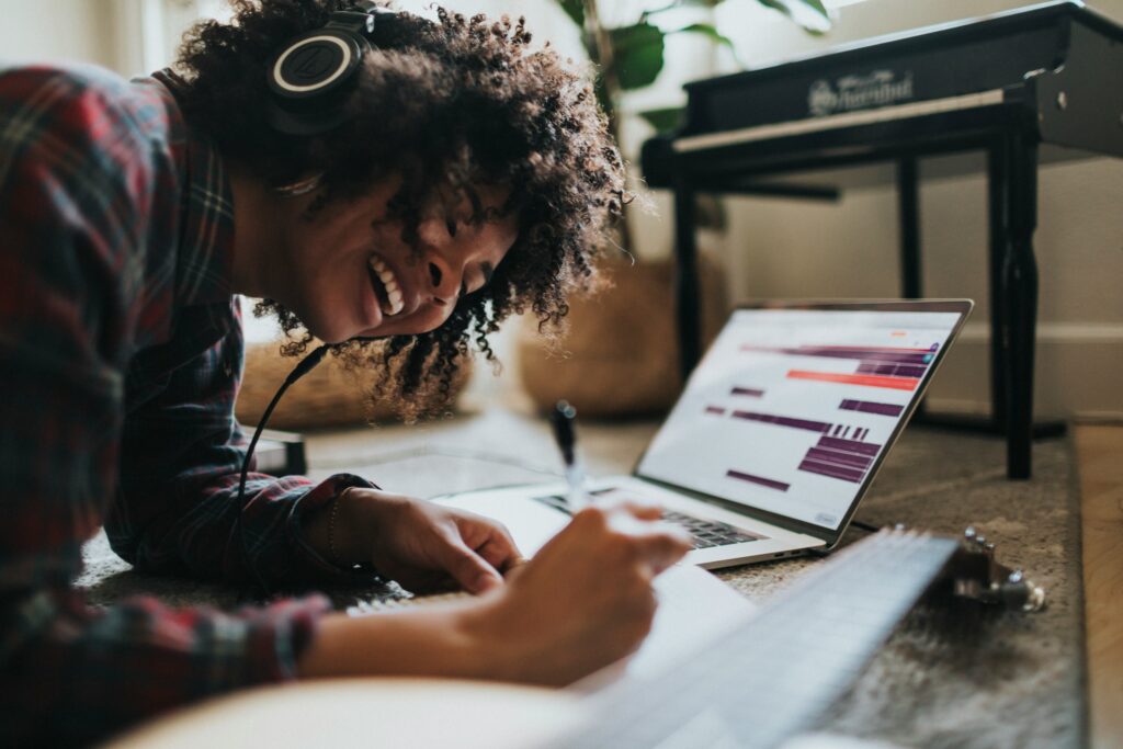 Woman smiling while writing in a notepad and wearing headphones