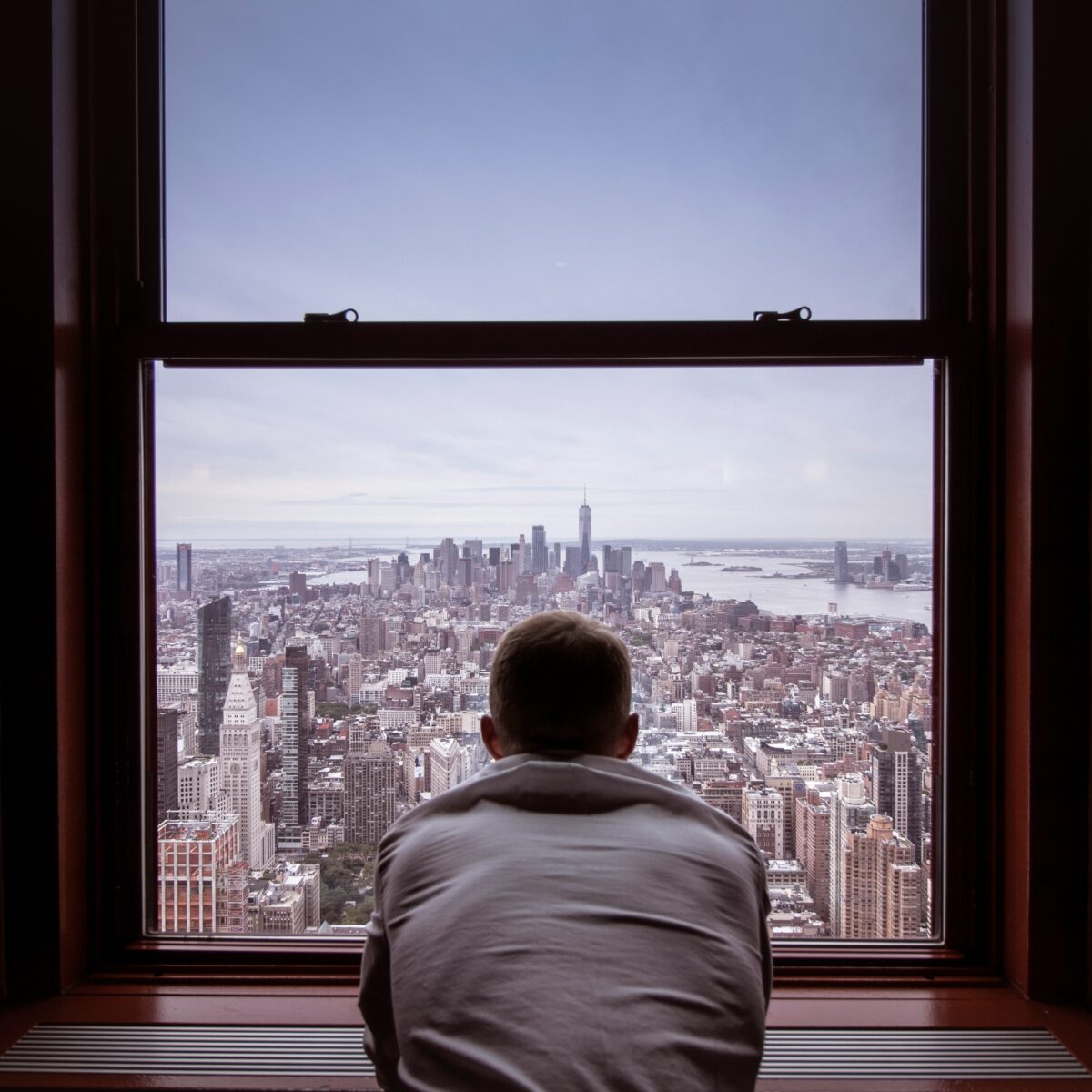 View of the Manhattan Skyline from behind a window. A man is looking out of the window with his back to the camera.