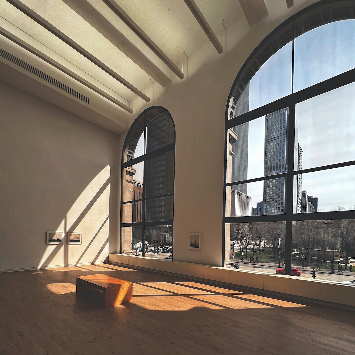 Sunlight streaming through huge windows in a large open-plan room, with views of a city skyline outside. Room is flooded with natural light.