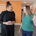 Screengrab from a video, of two women talking and smiling, while walking through the offices of social housing provider Wythenshawe Community Housing Group